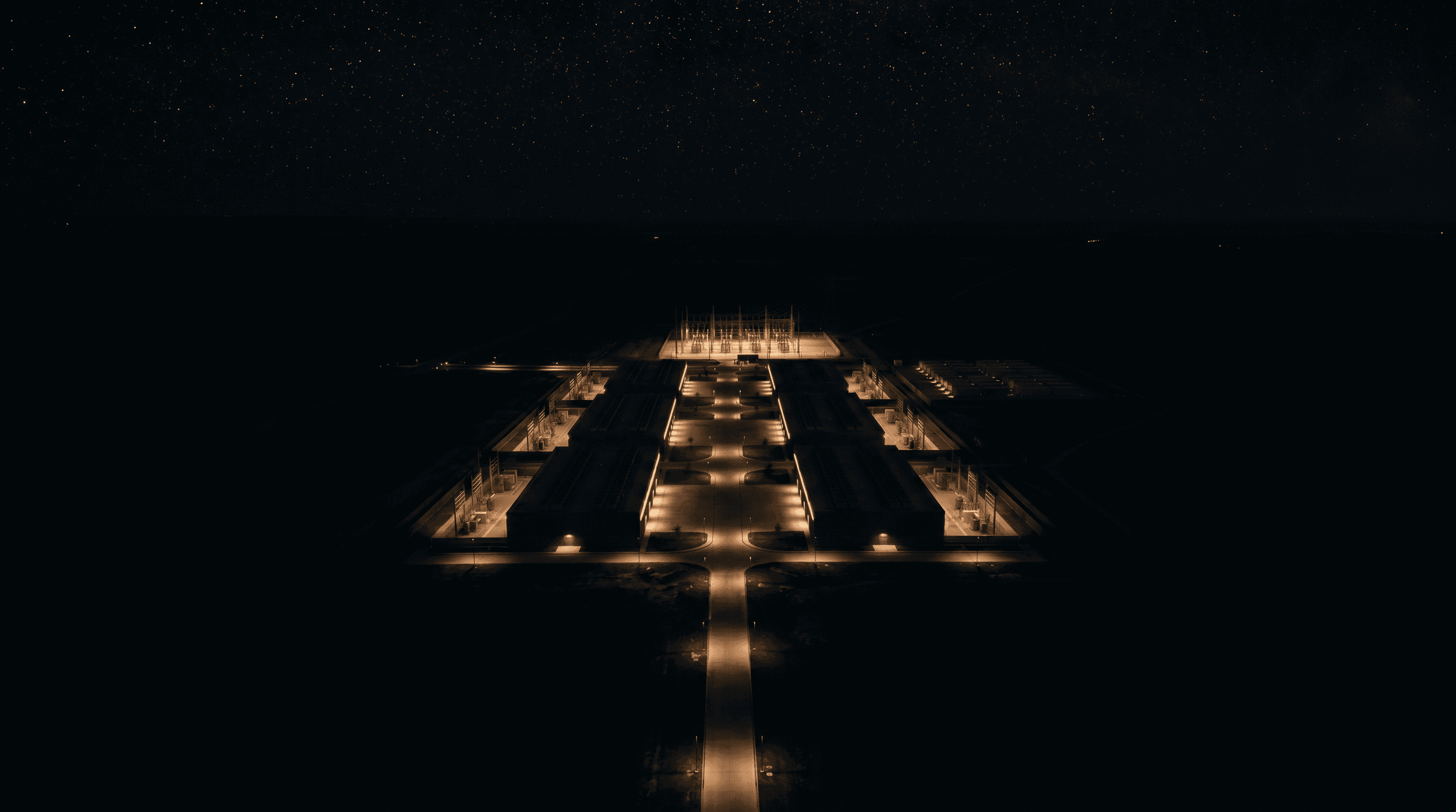 High-altitude aerial of the full campus at night, a constellation of ordered warm rectangles on dark land