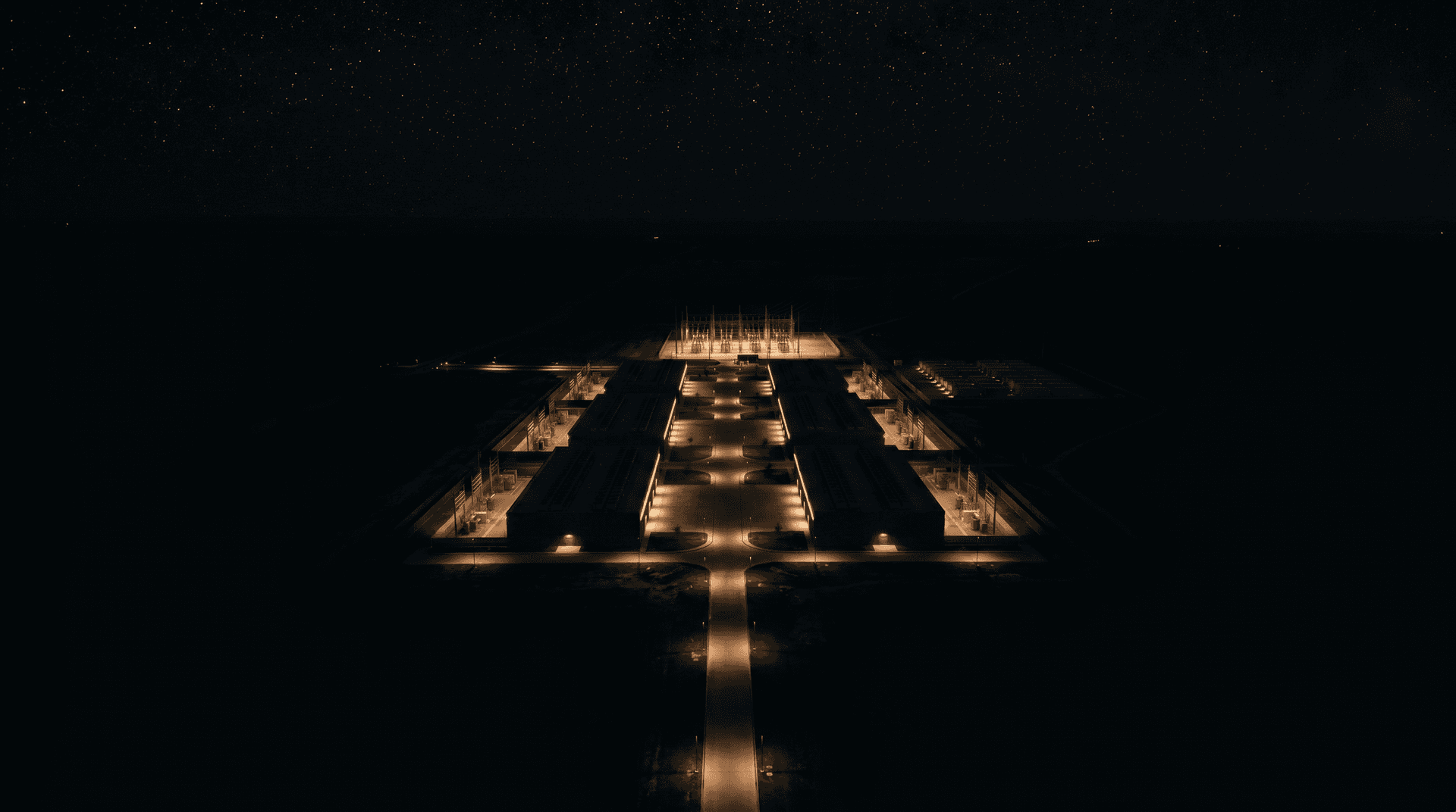 High-altitude aerial of the full campus at night, a constellation of ordered warm rectangles on dark land